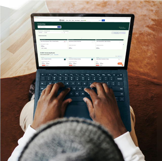 Person using a laptop with a website open on the screen, sitting on a wooden floor.